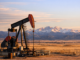 Oil pumpjack operating in a wide open western landscape near the Rocky Mountains at sunset